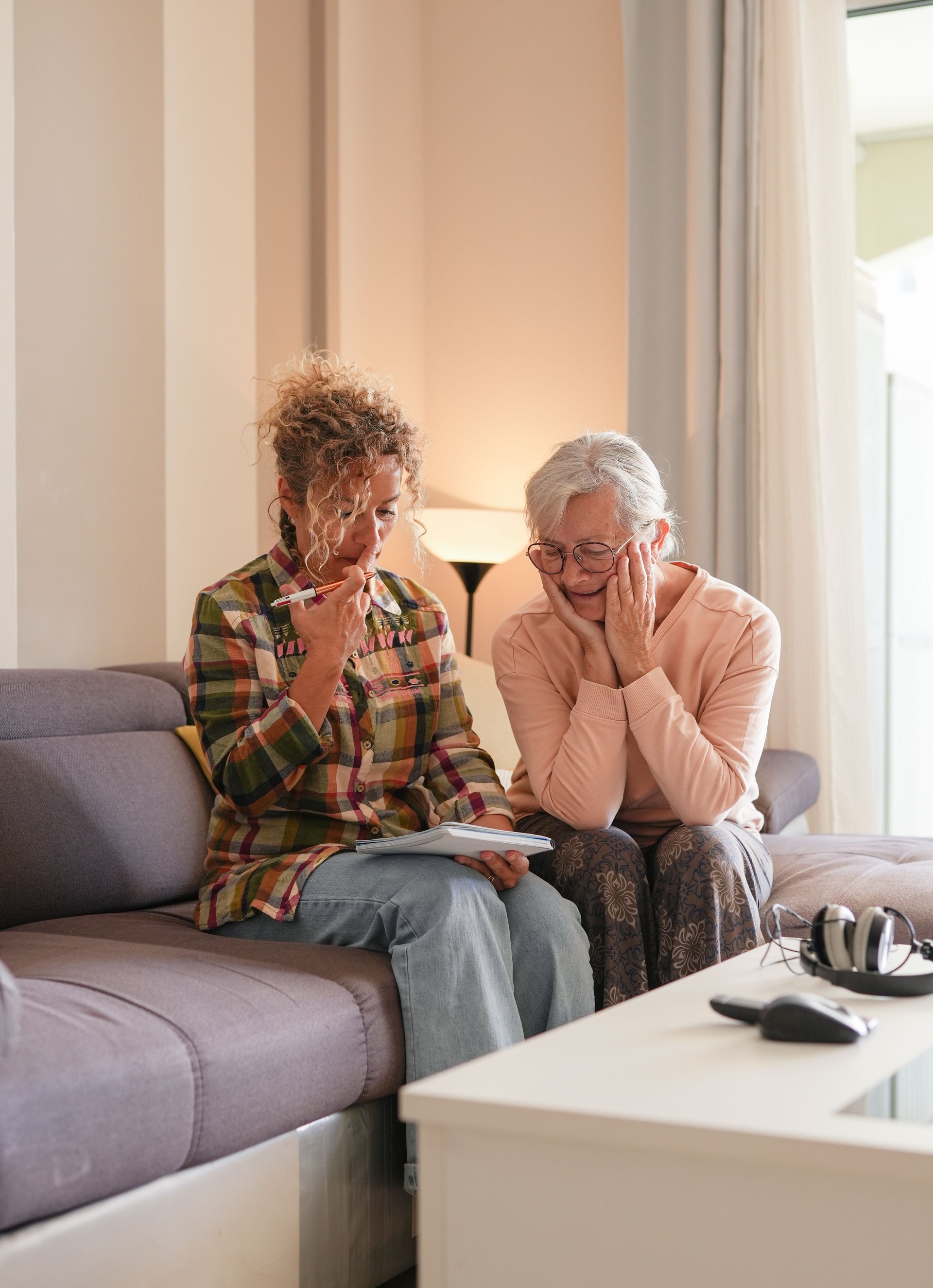 Smiling Senior woman and Caregiver Sharing a Moment sitting together on sofa at home. Concept of assistance and help to our elderly